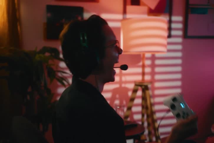 A young gamer in a headset celebrates winning his video game with an excited shout in his dimly lit room