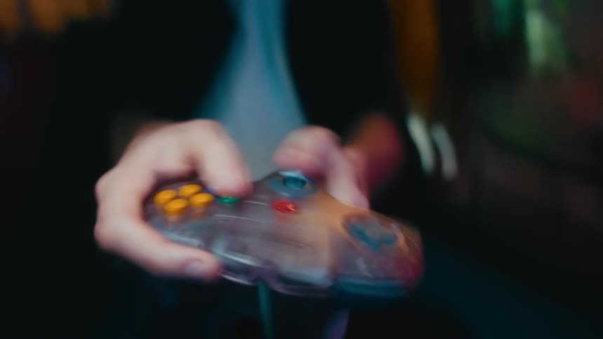 An intense, shaky close-up of a person's hands frantically playing a retro video game on a classic see-through controller