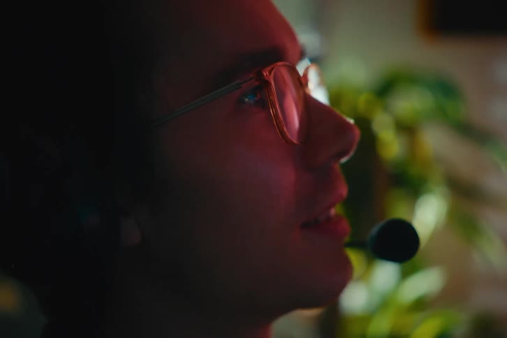 Intense profile shot of a young man with a gaming headset, his face lit by the colorful glow of the computer screen in the dark