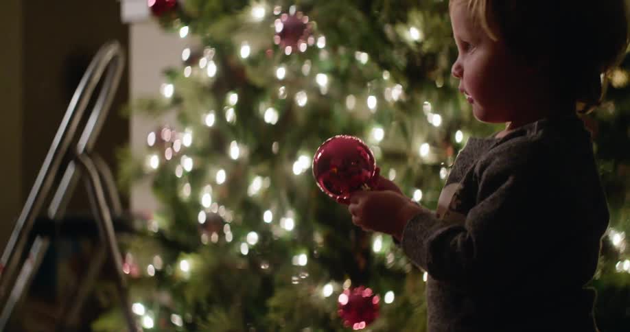 Child pulls a red christmas tree ornament out of a box