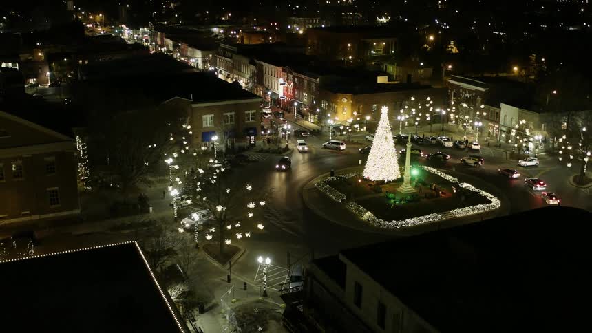 Cars drive around an illuminated christmas tree in a city