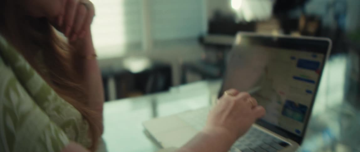 A businesswoman in glasses works from her modern home office, carefully analyzing a falling stock market graph on her laptop with a stylus