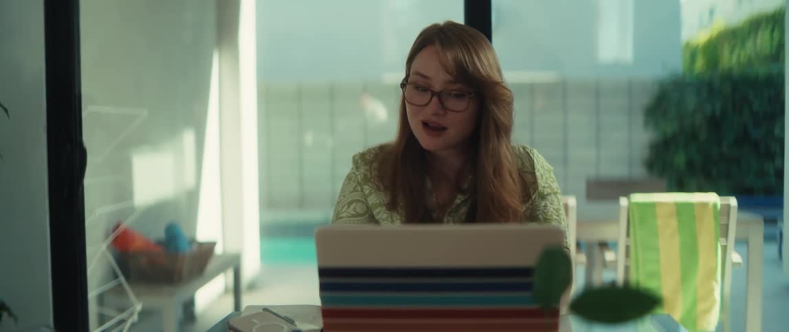 A woman with glasses works from her modern home, smiling and waving during a video conference on her laptop
