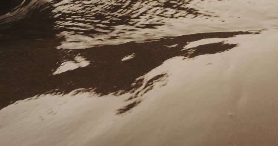 A mesmerizing close-up of sepia-toned water gently rippling before a small wave washes over the frame