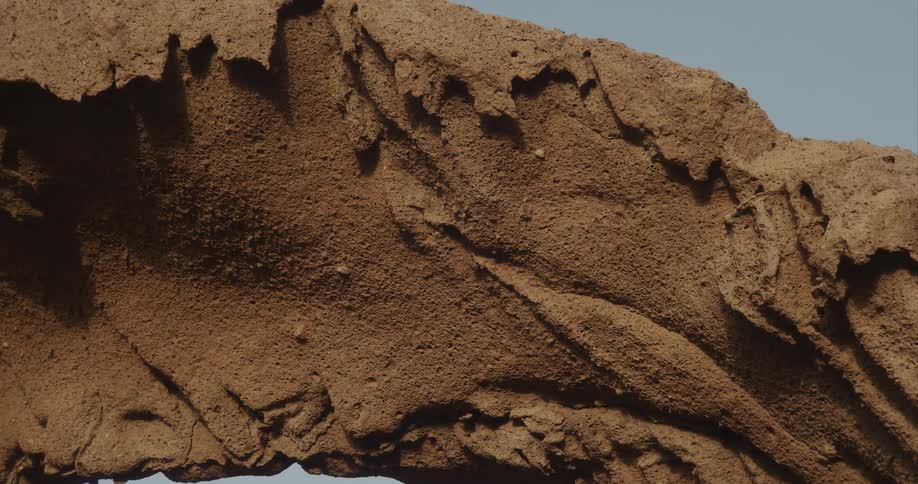 Detailed close-up of a rugged, weathered rock arch against a clear sky as the camera slowly zooms in