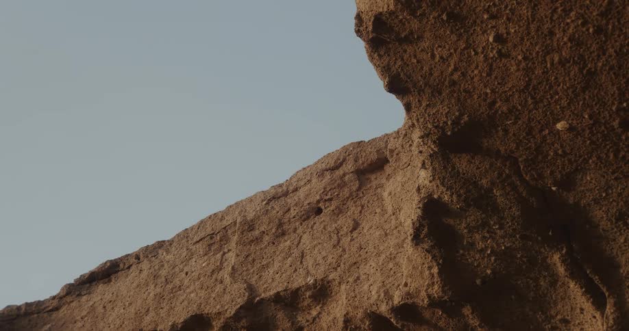 A timelapse captures the slow movement of shadows across a rugged, sandy rock formation under a clear sky