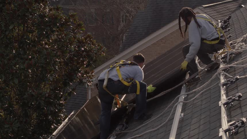 Two men wearing safety ropes on roof of house installing solar panels