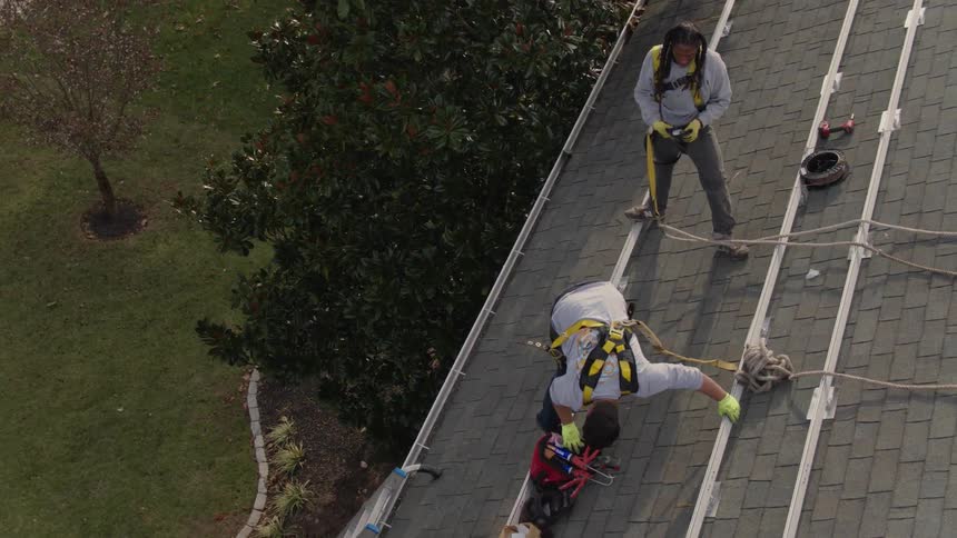 Two people are working on a roof with tools