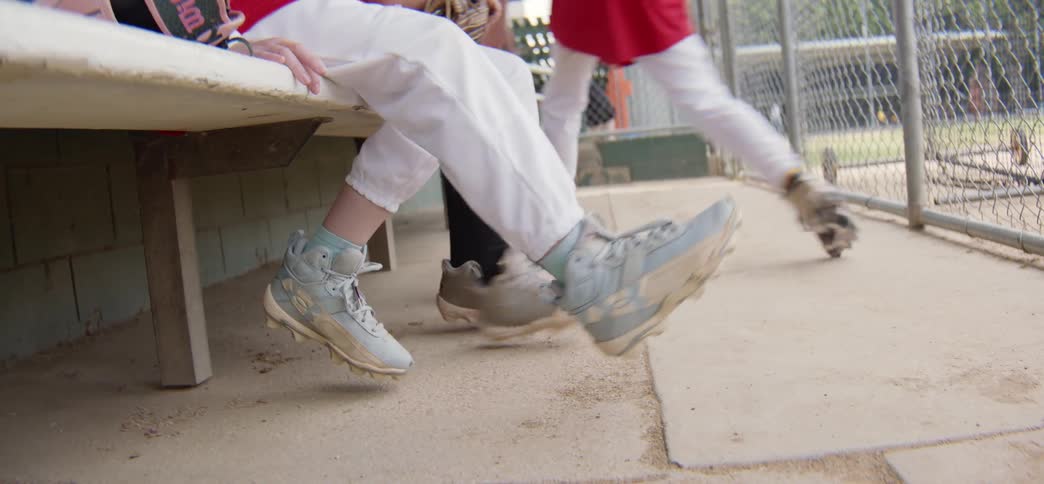 Young baseball players impatiently swing their legs on the dugout bench waiting for their turn to play