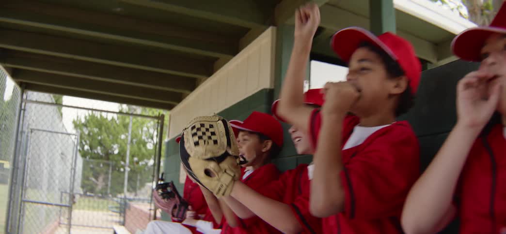 A youth baseball team enthusiastically cheers on their teammates from the dugout during a game
