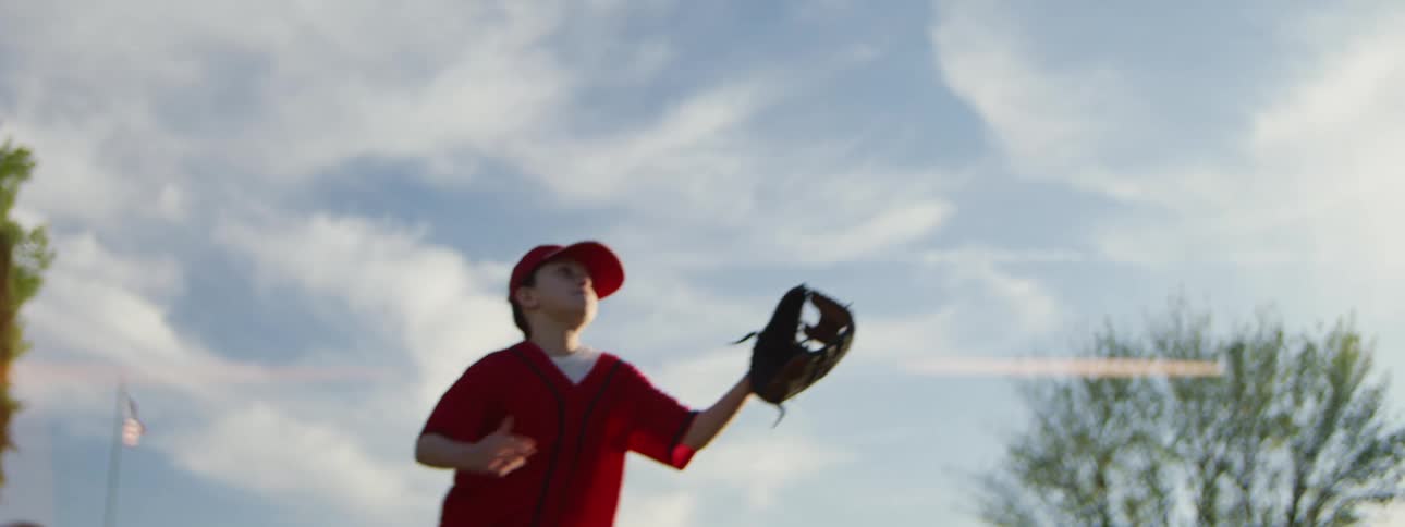A young female baseball player leaps in slow motion to catch a ball against a beautiful blue sky