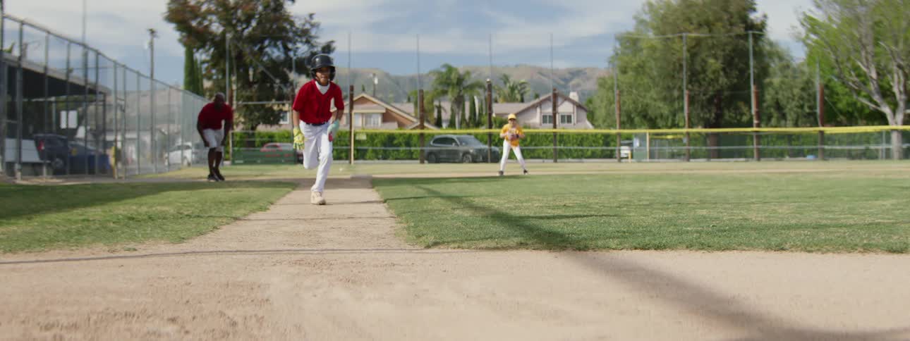 A determined young baseball player in a red jersey runs full speed before sliding safely into the base in dramatic slow motion