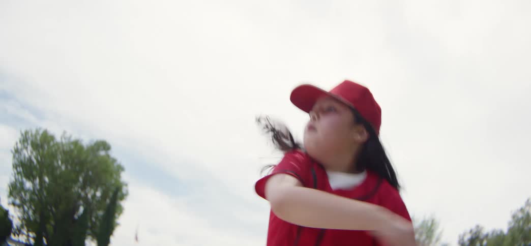 A young girl in a red uniform makes a determined catch and throw while playing baseball in slow motion