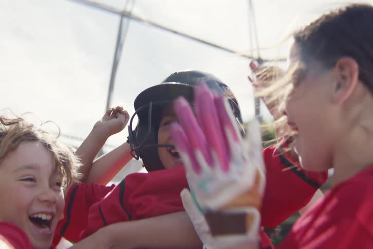 An excited little league baseball team celebrates in slow motion, lifting their teammate in triumph