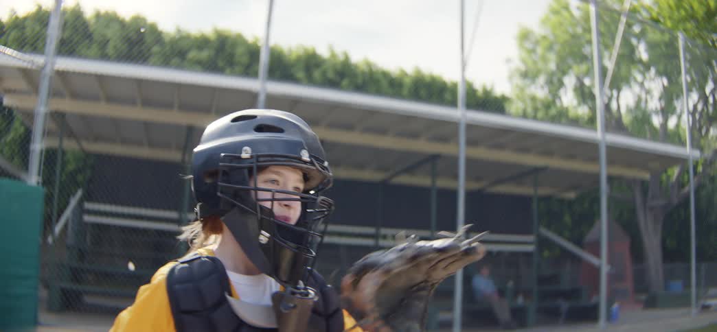 Slow motion close-up of a young girl in a catcher's uniform catching and throwing a baseball on a sunny day