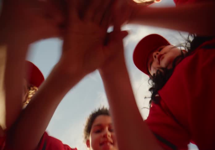 A team of young children in red uniforms cheer together in a huddle before a game, shot from a unique low angle perspective
