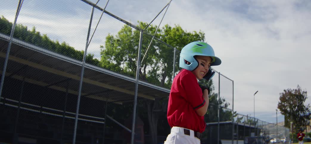 A little league batter hits a baseball in slow motion, smiles with joy, and runs to first base