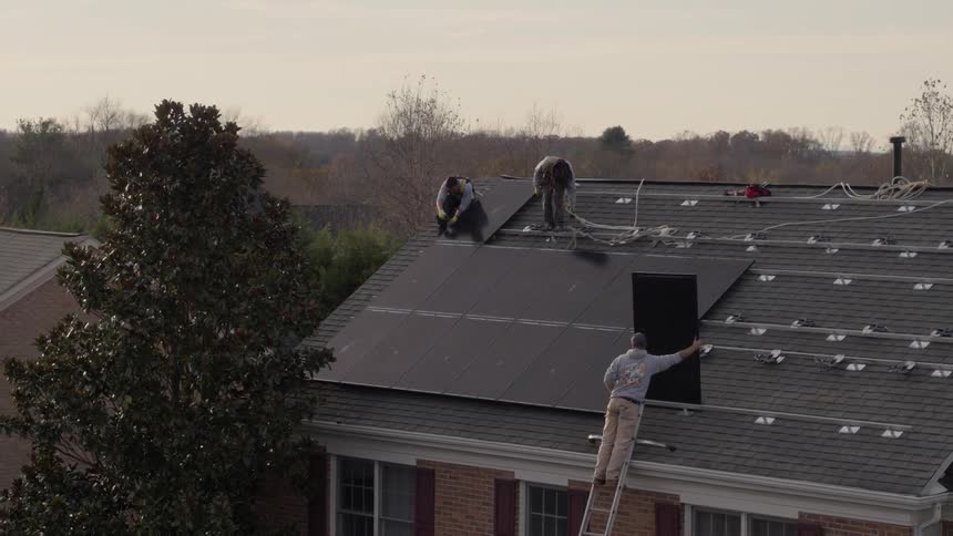 Workers are installing solar panels on a home roof