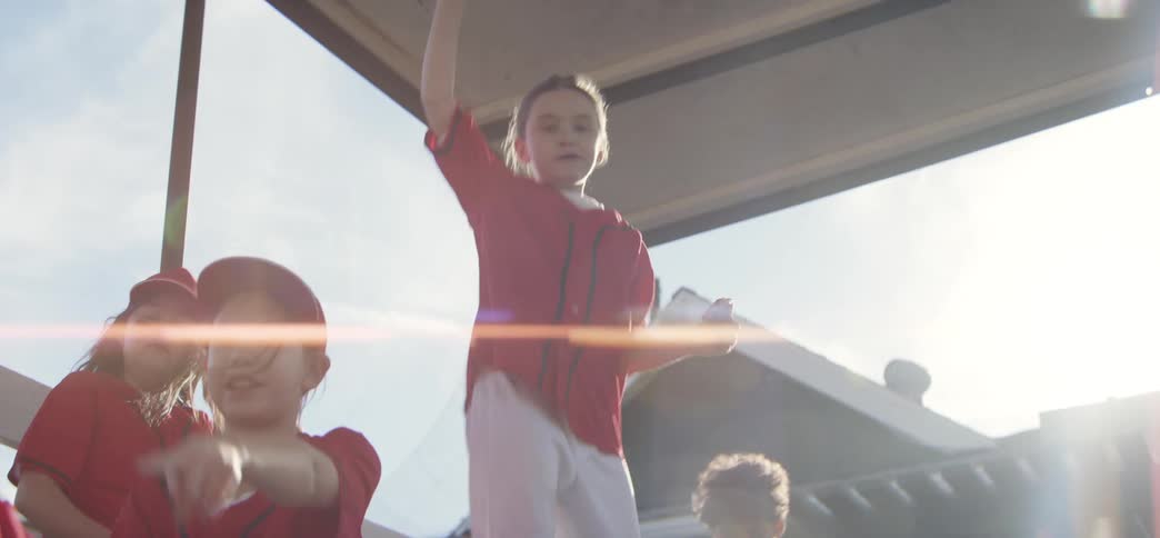 A slow-motion shot of a diverse youth baseball team celebrating and eating on the sunny bleachers after a game