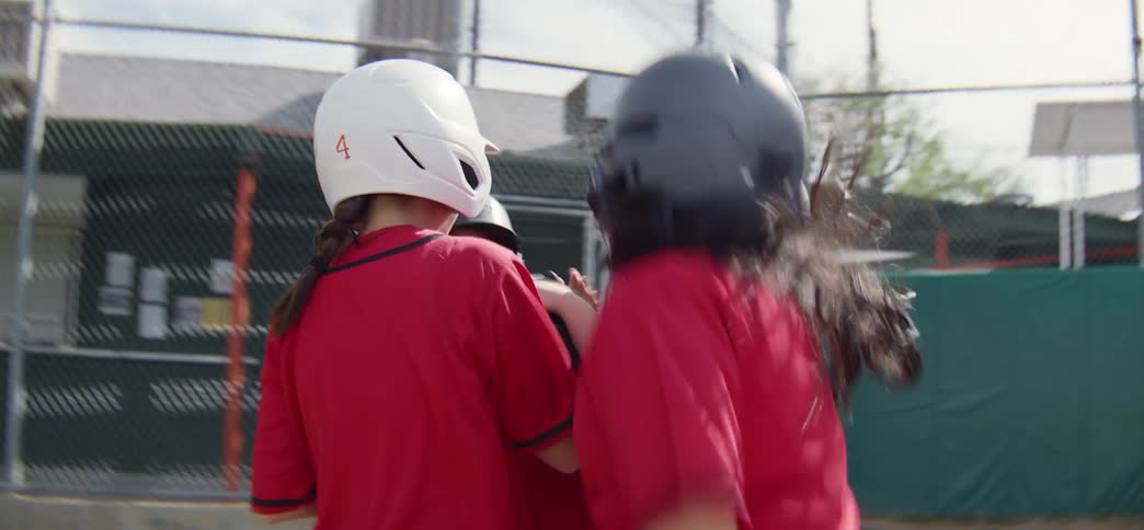 A young baseball player scores a run and is excitedly celebrated by their teammates in a slow-motion huddle