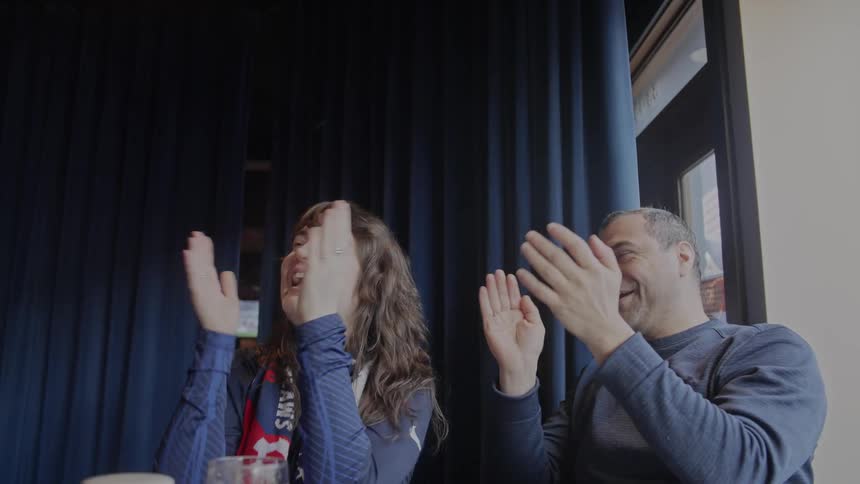 An ecstatic couple of sports fans cheer and clap in slow motion as they watch their team win at a pub