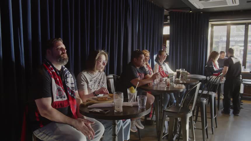A diverse group of dedicated sports fans wearing scarves intently watch a game together at a sports bar