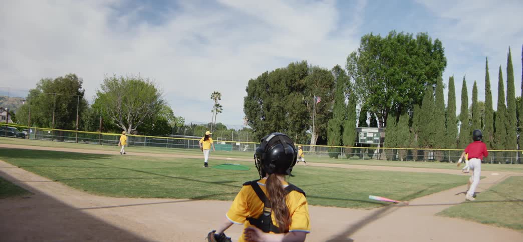 Slow motion shot of a youth baseball player hitting a pitched ball and running towards first base