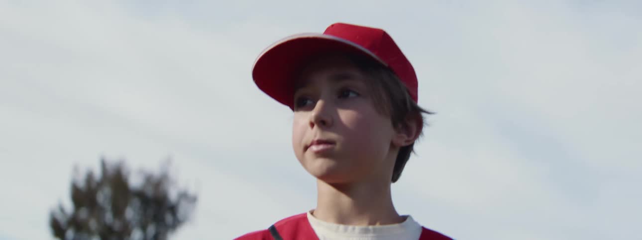 Slow motion close-up of a young baseball player in a red uniform as he throws and catches a ball with intense focus