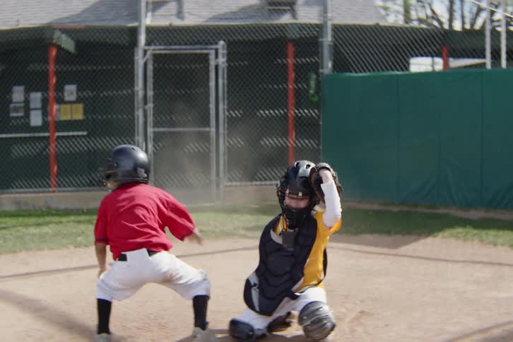 A determined little league player runs and slides safely into home plate, then celebrates the score with their cheering teammates in slow motion
