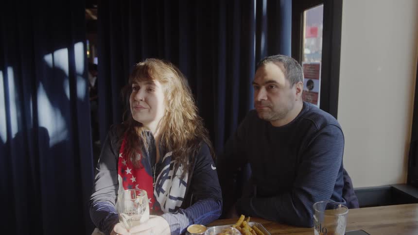 A happy couple enjoys a casual date at a restaurant, drinking and eating fries together while bathed in afternoon sunlight in slow motion