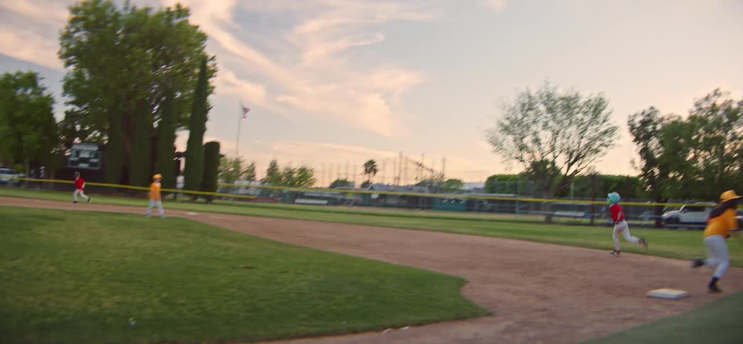 Little league players run the bases in slow motion during an exciting game on a classic American baseball field at sunset