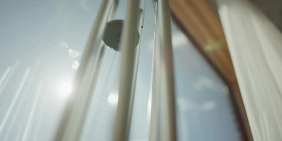 A serene, slow-motion close-up of a wind chime swaying gently in the bright sunlight