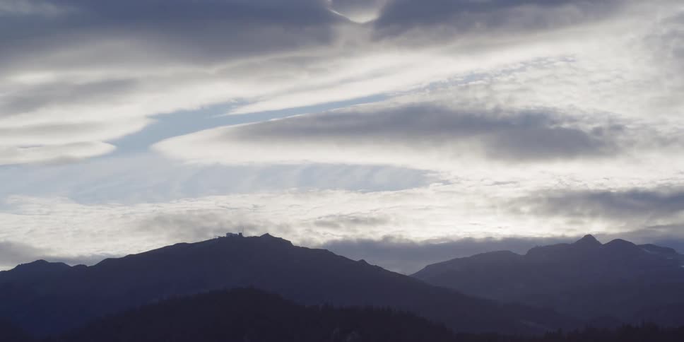 Dramatic clouds billow over a silhouetted mountain range during a stunning sunset timelapse
