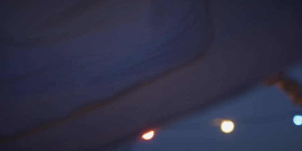 A dreamy slow-motion close-up of white laundry blowing gently on a clothesline against a deep blue dusk sky with soft string lights in the background