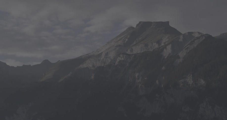 Sunlight fades across a majestic mountain peak as clouds drift by in a dramatic evening time-lapse