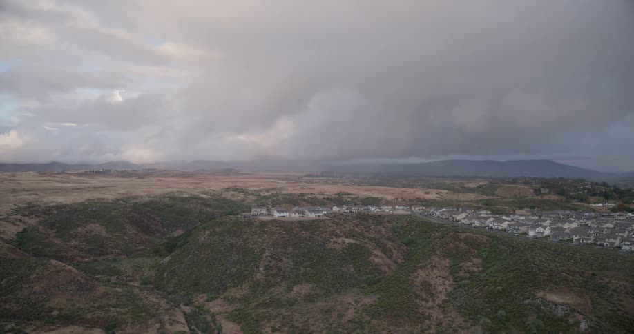 A wide aerial shot of a suburban neighborhood built into the rugged, hilly landscape under a moody, overcast sky