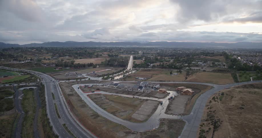 A static aerial view captures a new suburban housing development under construction next to a highway on a cloudy evening