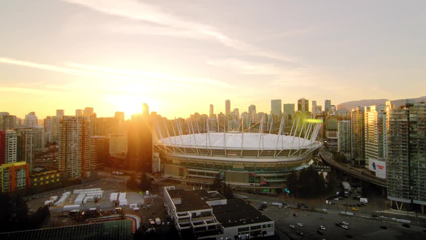 Stunning aerial shot pulling back from BC Place stadium, revealing the Vancouver city skyline bathed in golden sunset light and False Creek below