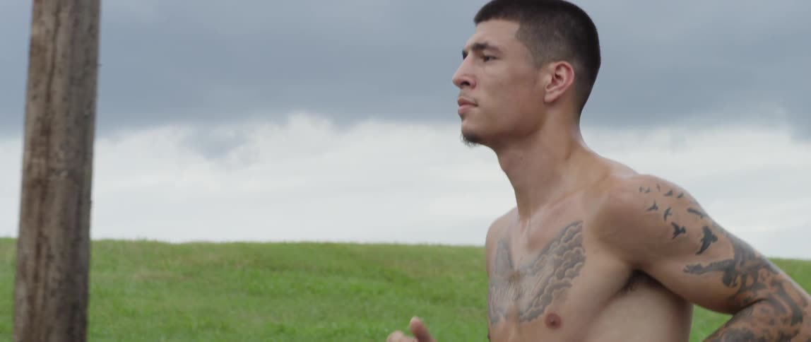 A tattooed man runs beside a grassy hill