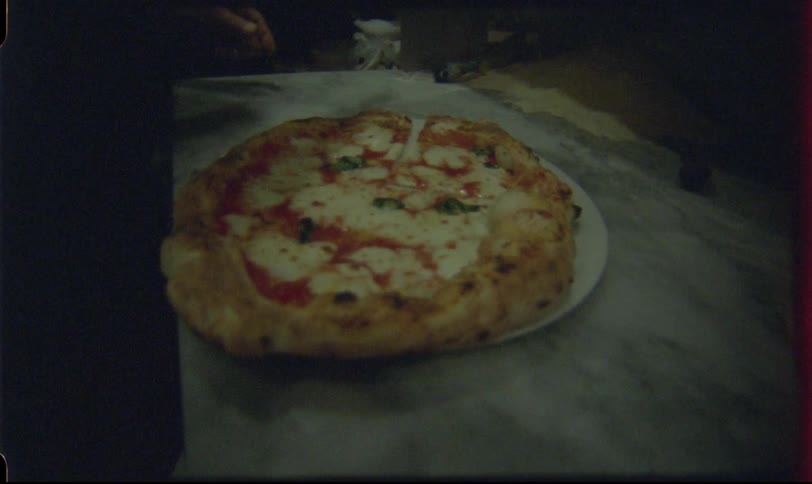 A freshly baked margherita pizza is sliced and presented to the camera in this vintage-style footage