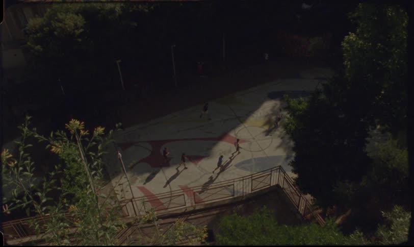 Authentic Super 8 film captures a nostalgic high-angle view of children playing in a single patch of sunlight on a colorful urban playground