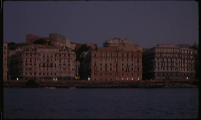 A vintage film-style view of a historic European city waterfront glowing with lights at dusk