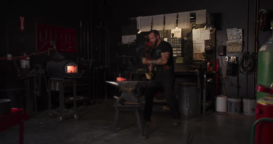 A muscular blacksmith hammers a piece of glowing hot metal on an anvil in his dark forge