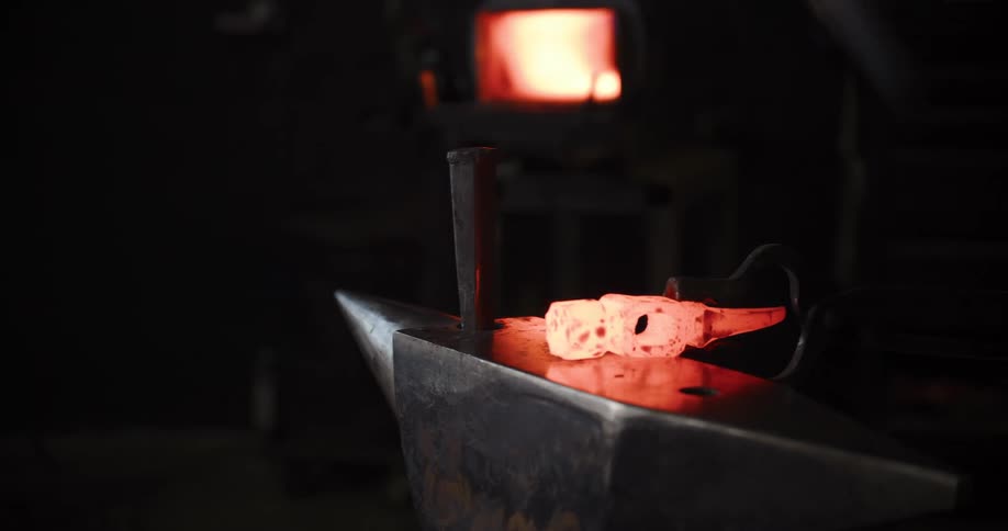 A blacksmith forges a pair of metal dice, removing the glowing material from the furnace and hammering it into shape on an anvil