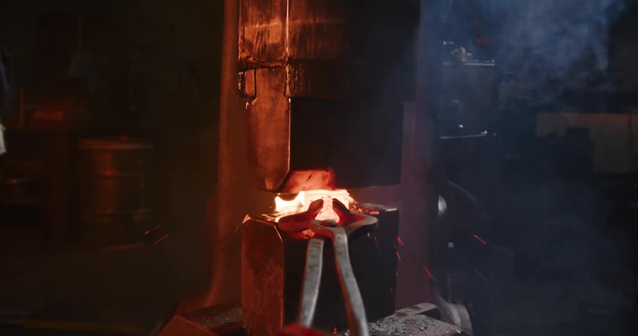 Dramatic slow motion shot of a power hammer forging red-hot metal, causing an explosion of sparks and fire