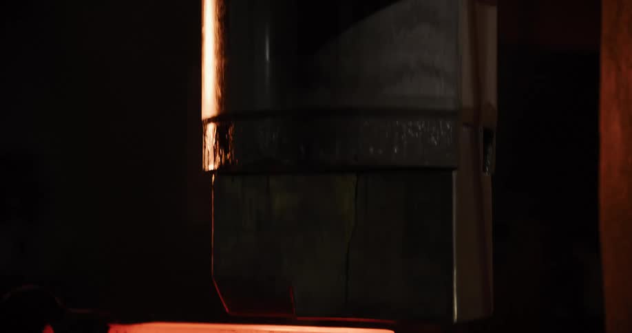 An industrial forging press hammers a piece of glowing hot steel in a shot that reveals the intense heat and power of the machine