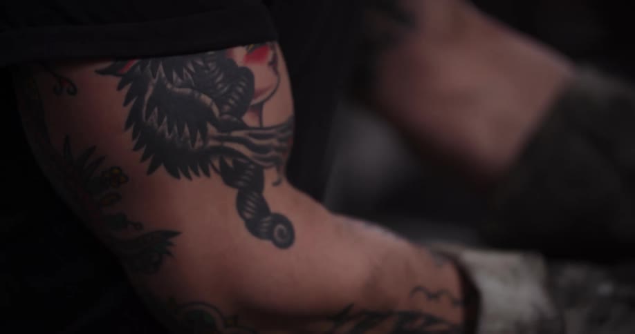 Cinematic slow-motion close-up of a tattooed craftsman's face tilting down to his gloved hands holding tongs