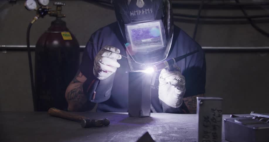 A craftsman wearing a protective helmet expertly welds a metal seam, creating a bright flash of light and sparks