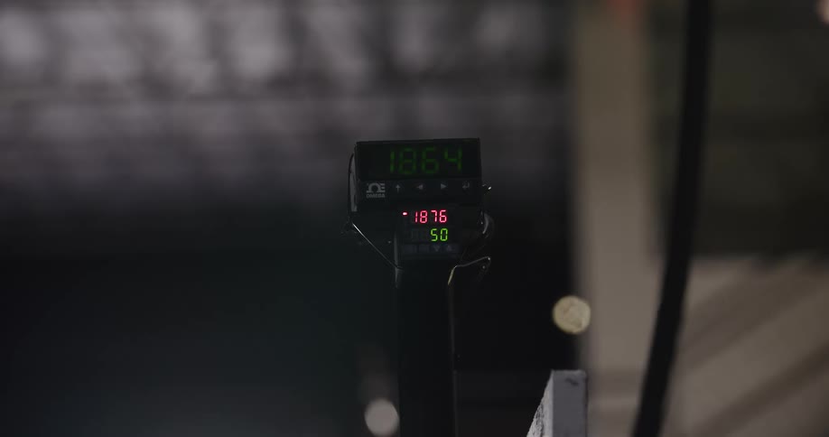 A close-up of a digital temperature gauge with glowing numbers counting up in a dark, hazy workshop