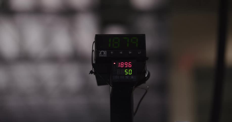 A close-up of a digital display shows red and green numbers fluctuating on a timer in a workshop